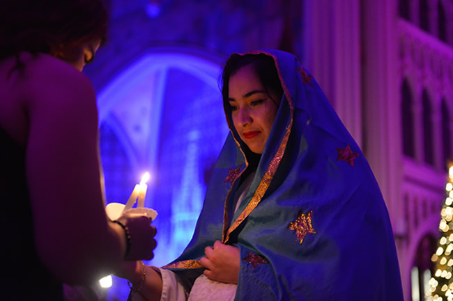 Female student dressed as Mary lighting candle