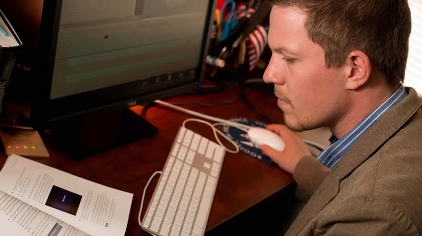 Male Student looking at textbook while on computer