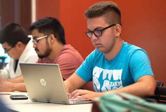 Male sitting at talbe typing on laptop 