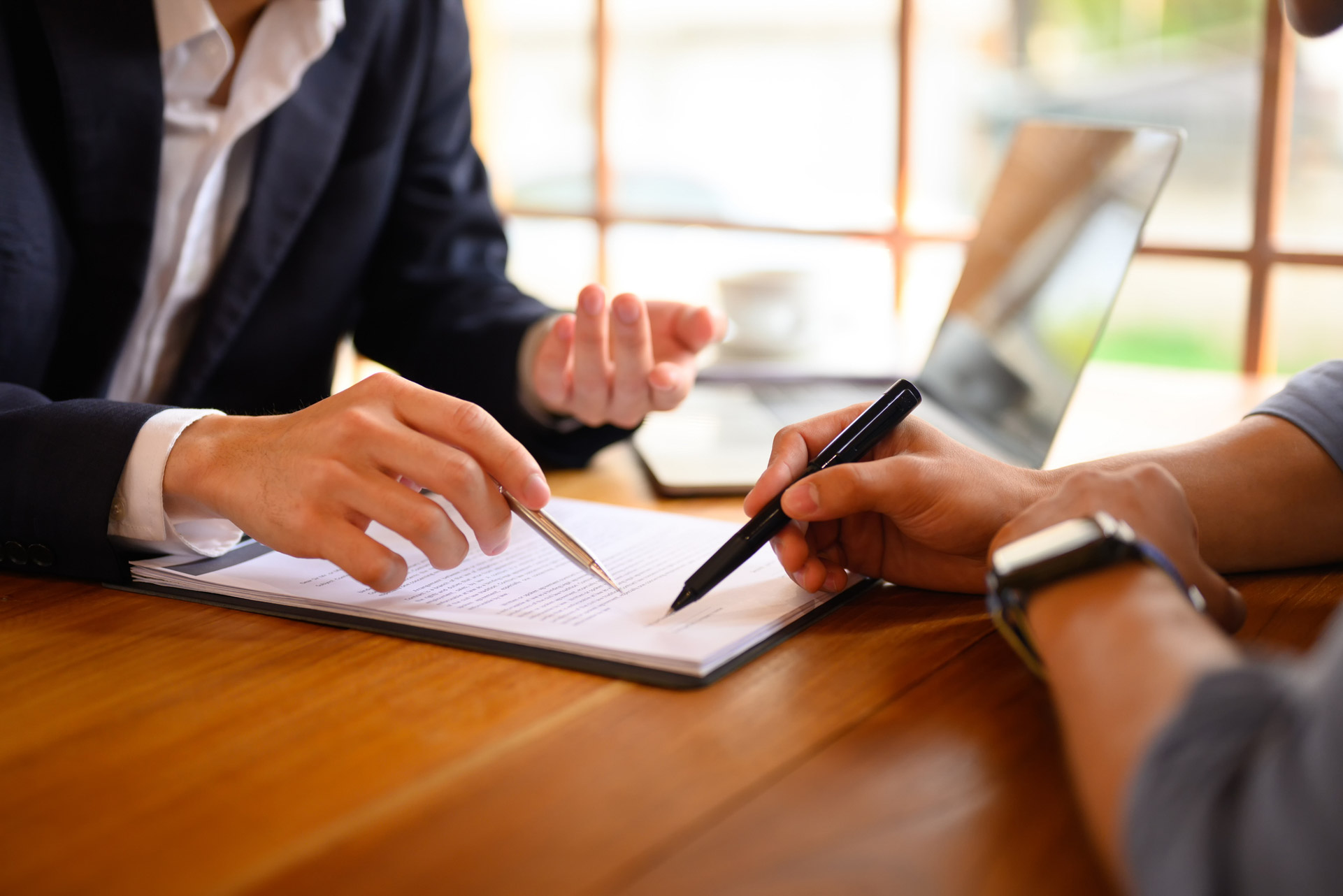 Business professional pointing at a contract, guiding a client on where to sign, using the practical applications of a business management degree.