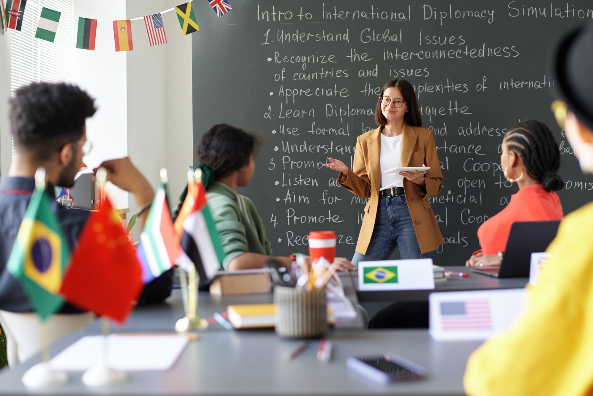 Smiling international business teacher greeting adult bilingual certification students in a classroom.