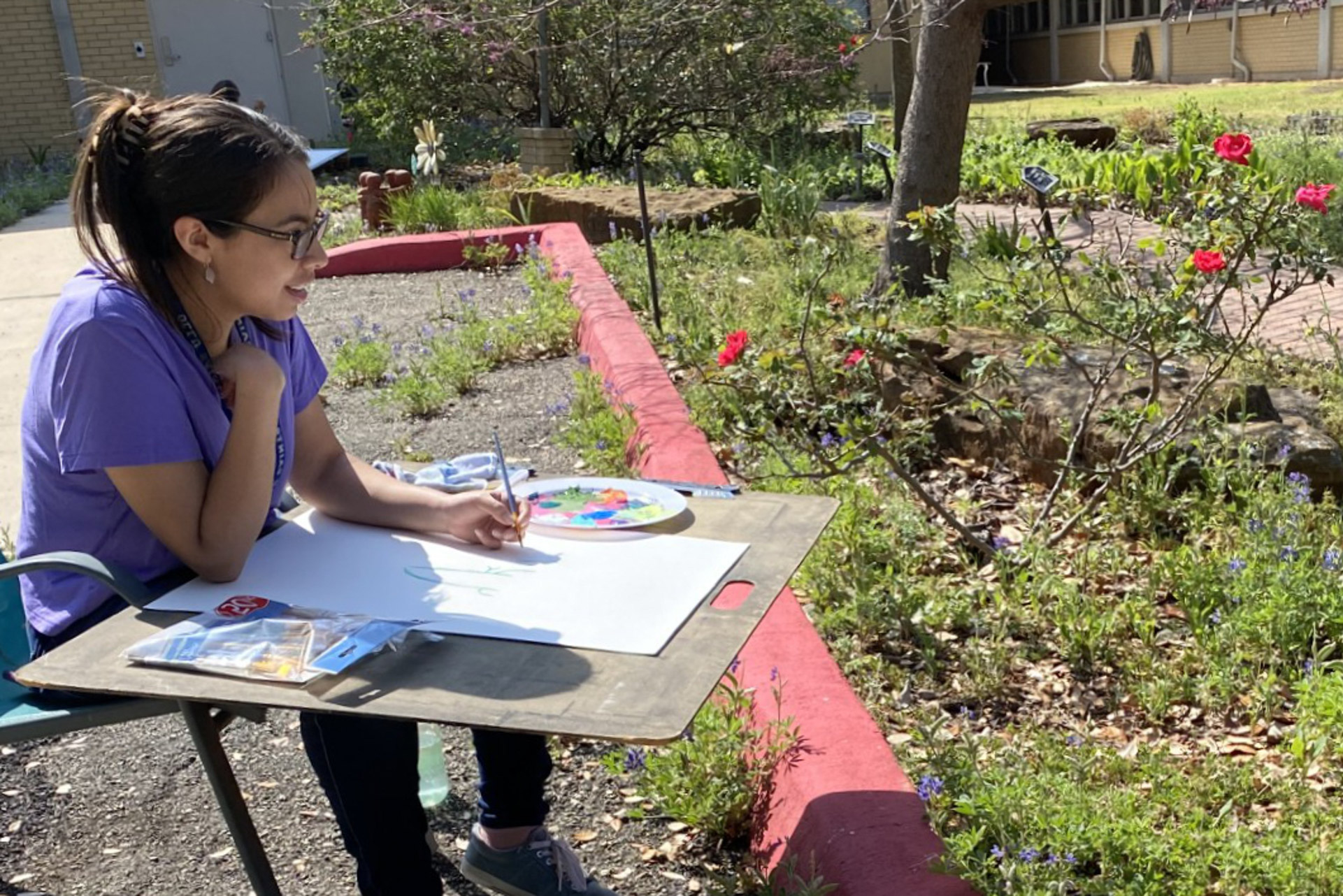 Visual and New Media Arts student at Our Lady of the Lake University painting floral artwork outdoors in the Martha Rose Lange Peace Garden.