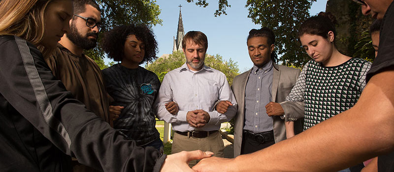 Staff member and students holding hands outside praying