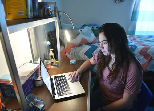 Female student using laptop in room on desk
