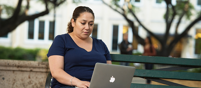 Female student sitting on bench with laptop