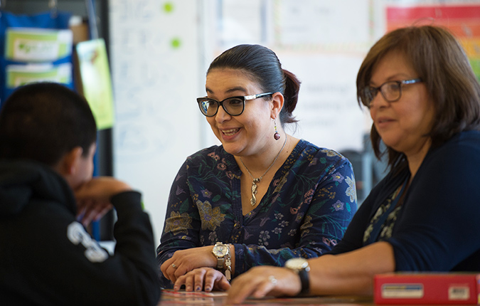 Two students sitting talking with child in classroom