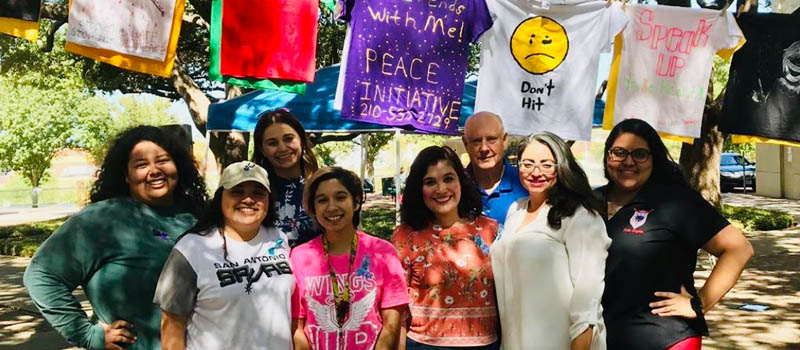 Counseling services staff members stand in front of T-shirts during clothesline project