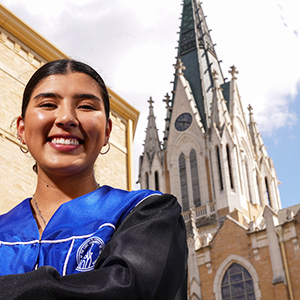Student smiling in regalia with chapel in the background