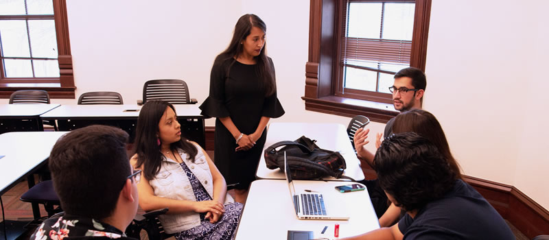 Group of students talk with professor in classroom