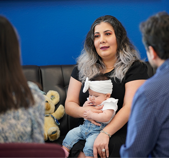 Mother holding child speaking with student and professor